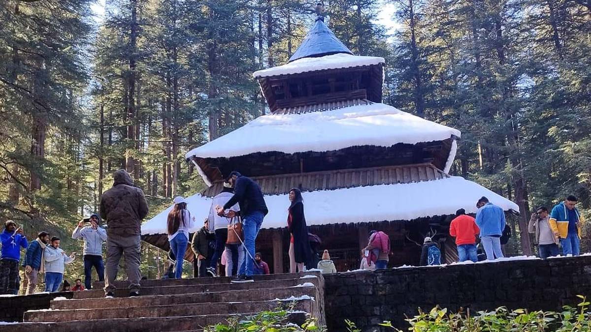 a group of people standing on stairs outside Hidimba Devi Temple with snow on the roof