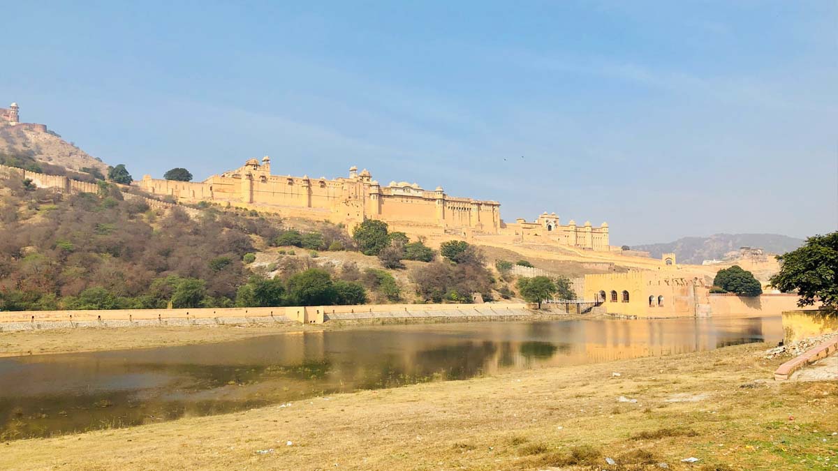 a large building on a hill with a body of water with Amer Fort in the background