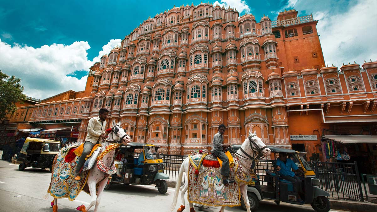 a group of people riding horses in front of a large building which is Hawa Mahal