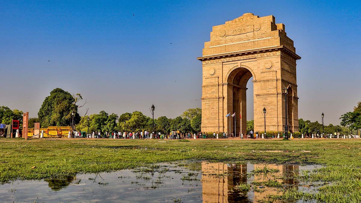 a large stone arch with people in the background with India Gate in the background