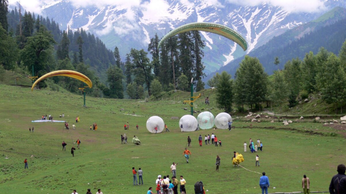 a group of people on a field with large white balls with Solang Valley in the background