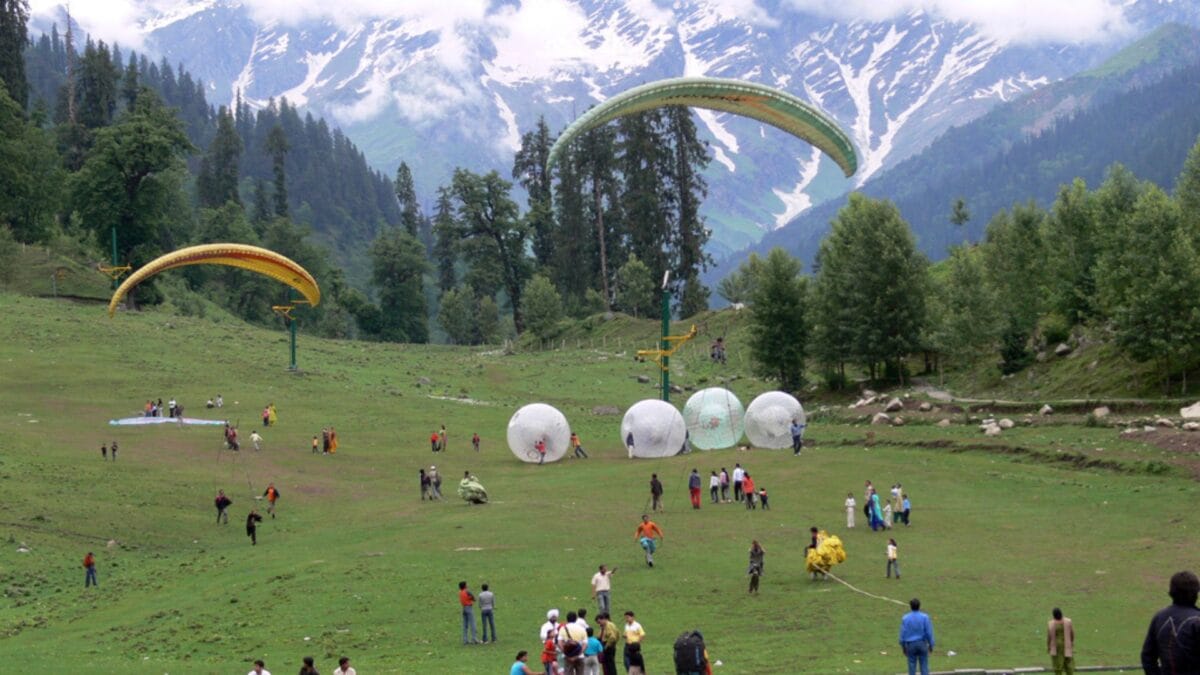 a group of people on a field with large white balls with Solang Valley in the background