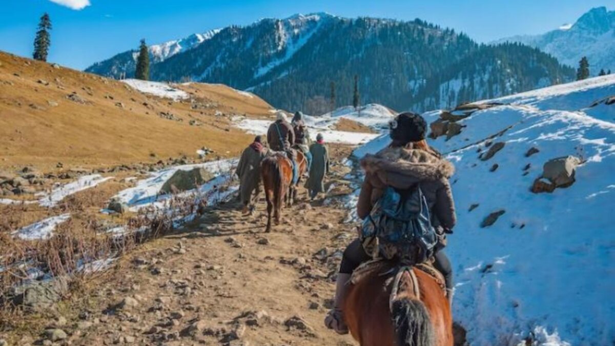 people riding horses on a dirt path, snow and mountains in Pahalgam